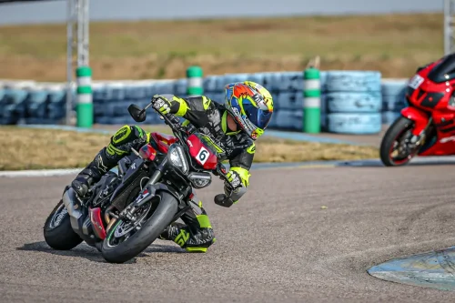 Motorradfahrer mit neon-gelber Lederkombi von 4SR und Scorpion Helm auf der Rennstrecke mit einer Triumph Street Triple 765RS. Er fährt Schräglage mit dem Knie auf dem Boden und schaut Richtung Kurvenausgang