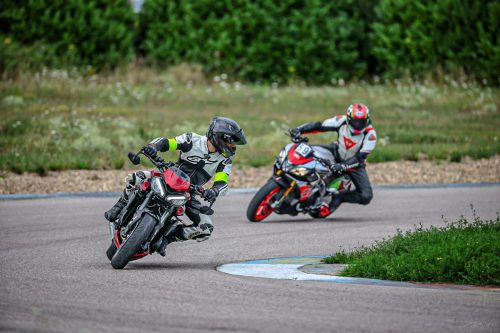 Motorrad-Instruktor mit seinem Teilnehmer auf der Rennstrecke. Der Instruktor schaut zurück, während der Teilnehmer den Kurveneingang im Hanging-Off anfährt und weit in die Kurve schaut