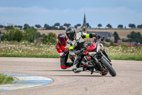 Motorrad-Instruktor mit einem Teilnehmer auf der Rennstrecke mit starker Schräglage im Hanging-Off und dem Knie fast auf dem Boden